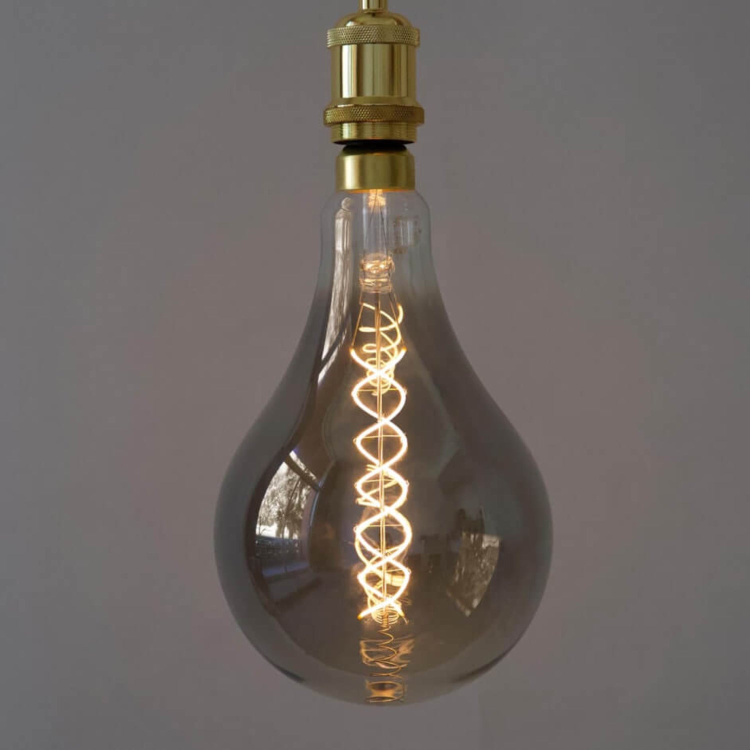 Close-up of illuminated smoky glass LED bulb with spiral filament and brass pendant fitting.