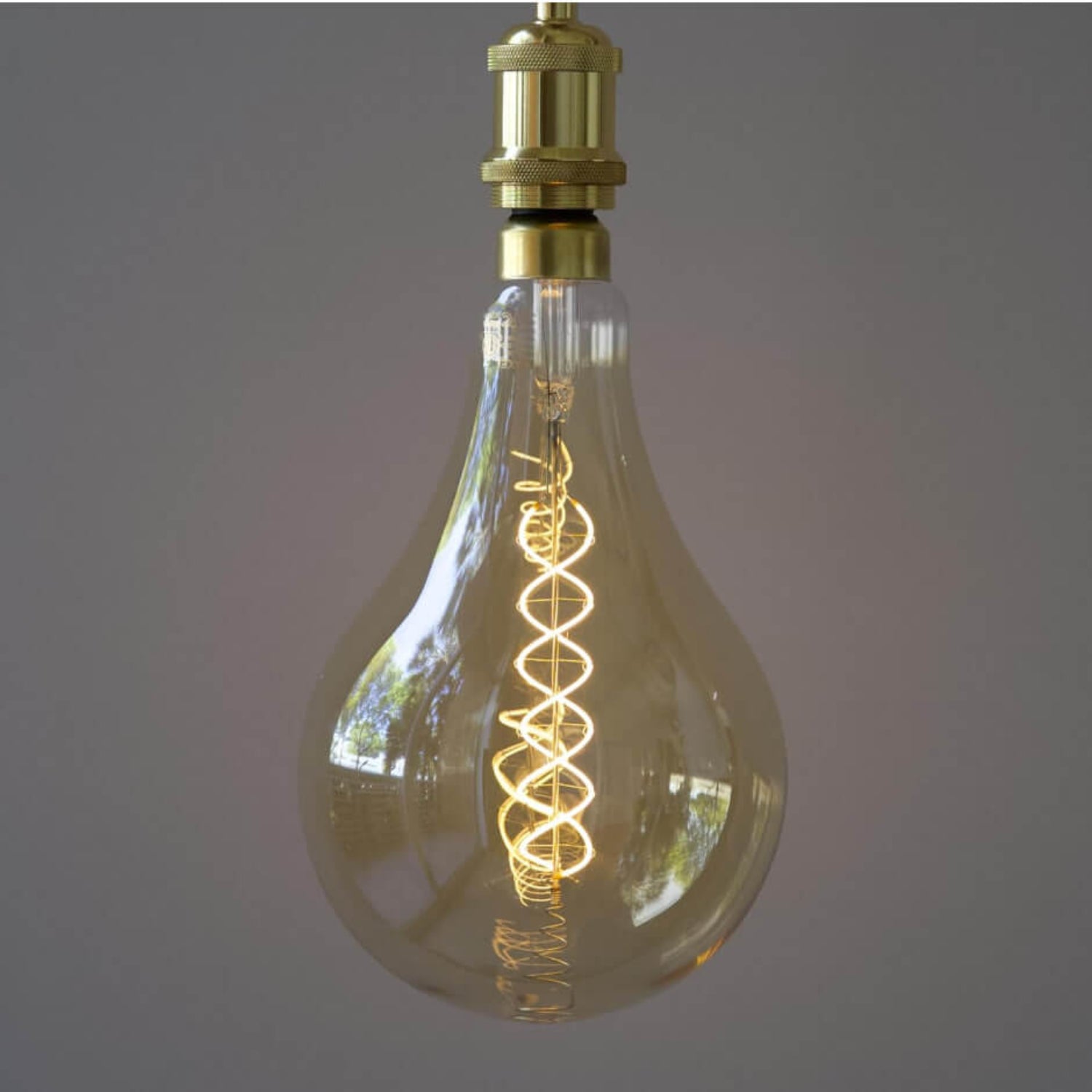 Lit Luxel oversized LED Edison bulb with visible warm white spiral filament and brass socket in a dimly lit room.