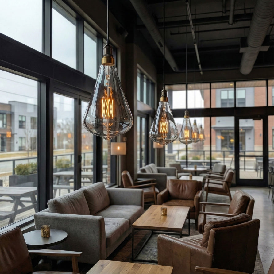 Modern interior with large windows, gray sofa, brown chairs, and hanging light bulbs.