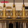 Four vintage-style light bulbs hanging above a table with a blurred cityscape background, featuring the Luxel brand.